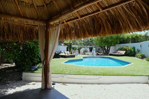 A pool area with a thatched roof, a small pool, and surrounding greenery. - ALOE B&B (Oranjestad)
