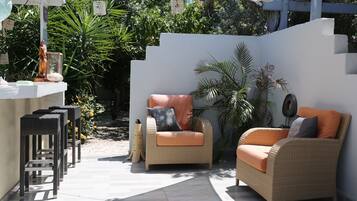 A patio area with wicker furniture, a bar counter, and lush greenery.