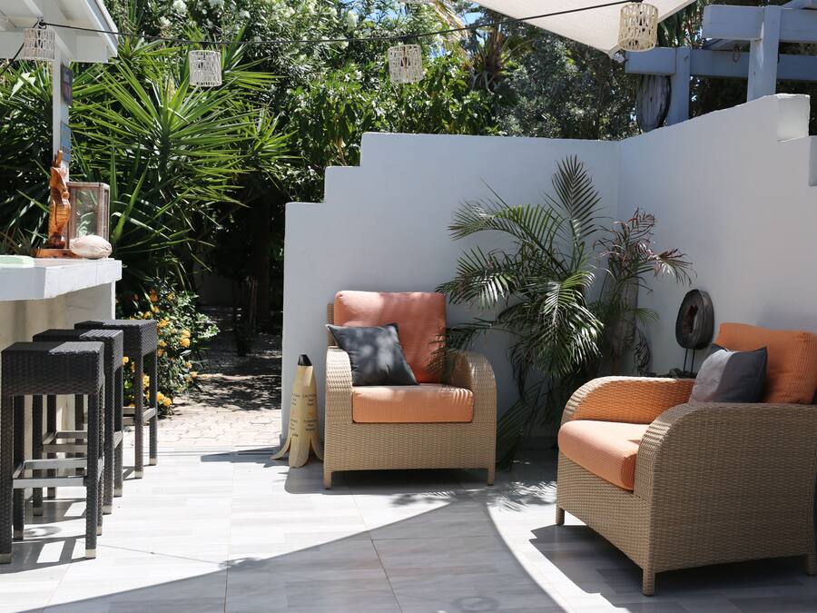 A patio area with wicker furniture, a bar counter, and lush greenery.