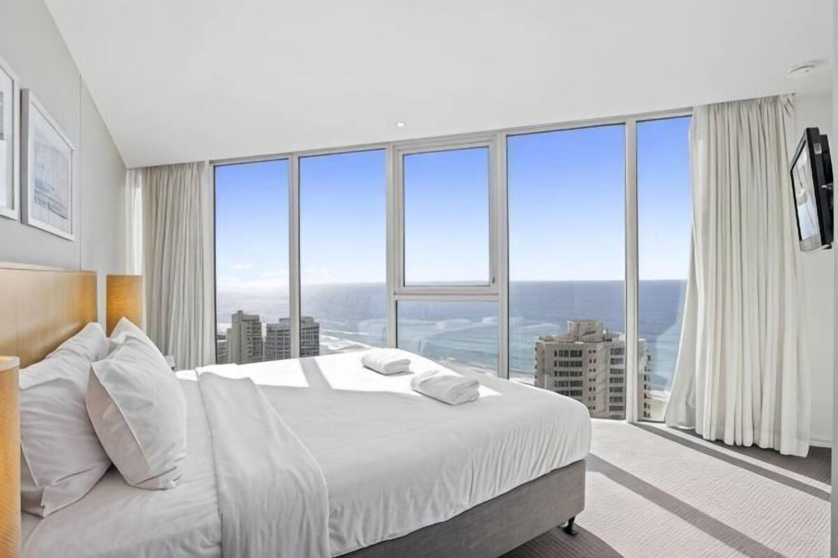 A hotel room with a large bed, a city view, and a flat-screen TV mounted on the wall.