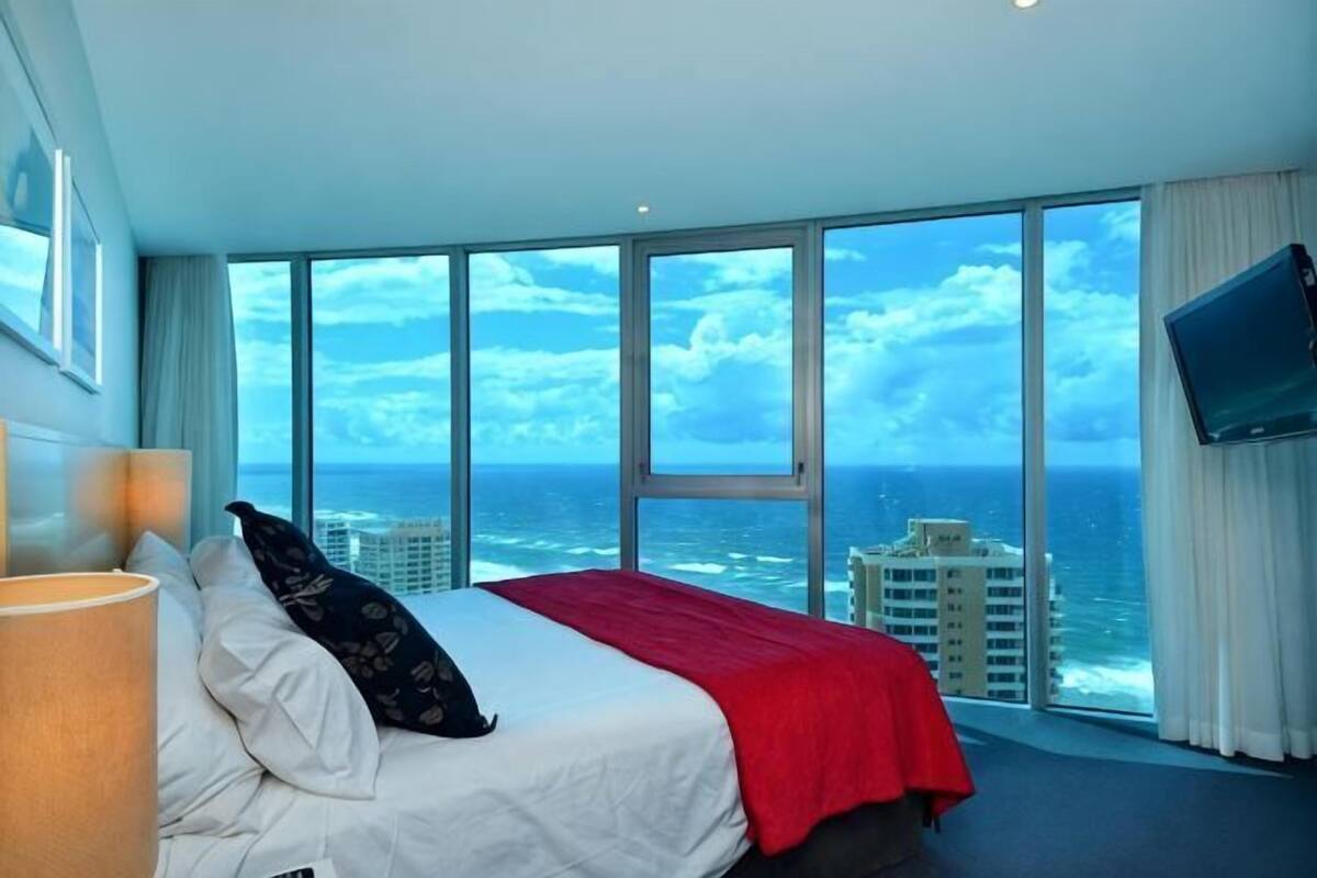 A hotel room with a large bed, a TV, and a view of the ocean.
