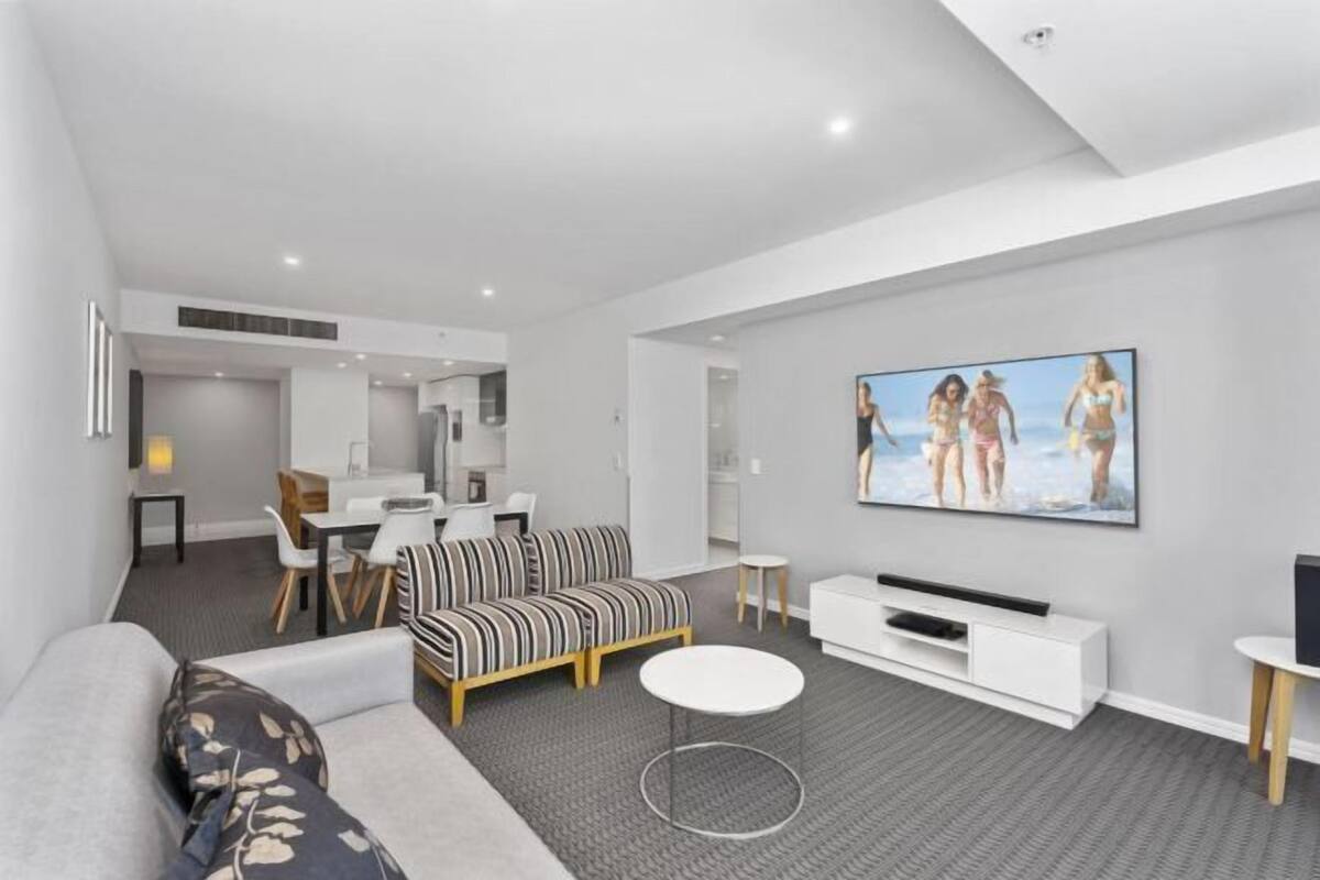 A modern living room with a sofa, a coffee table, a TV, and a dining area with chairs and a table.