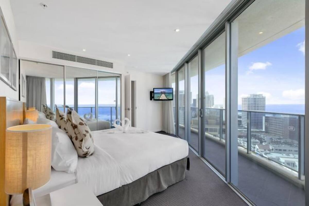 A modern hotel room with a large bed, a TV, and a balcony with a city view.