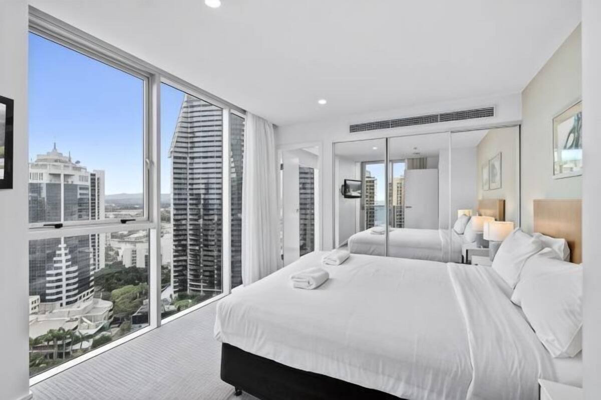 A modern hotel room with a large bed, a view of the city, and a large window.