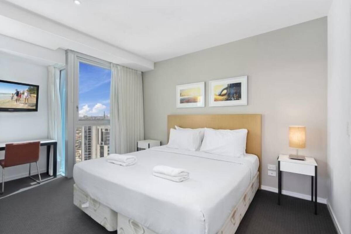 A hotel room with a large bed, a desk, a chair, a TV, and a window with a view.