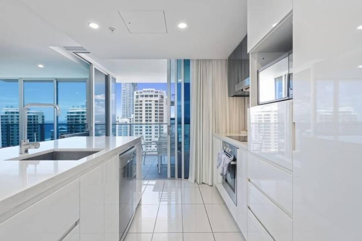 A modern kitchen with a large island, a view of the city, and a balcony with a cityscape.