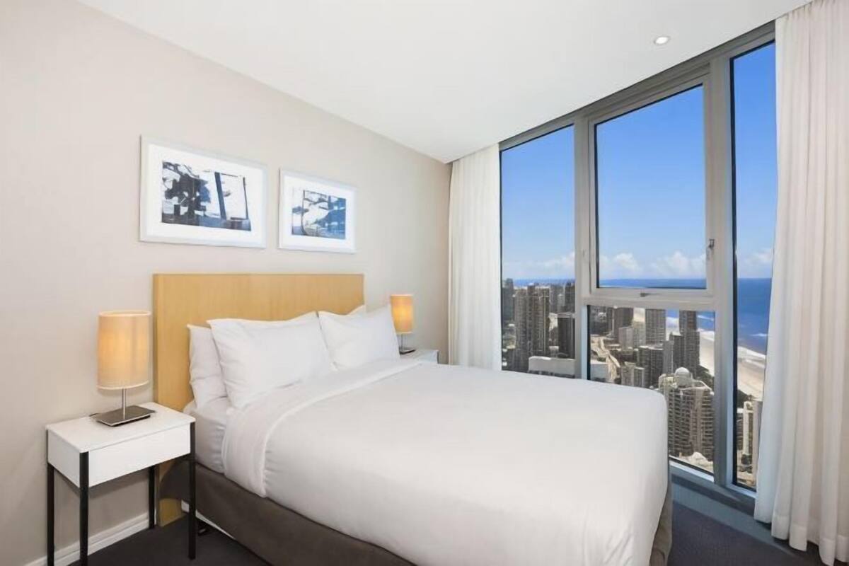 A hotel room with a large bed, two bedside tables, a city view, and framed pictures on the wall.