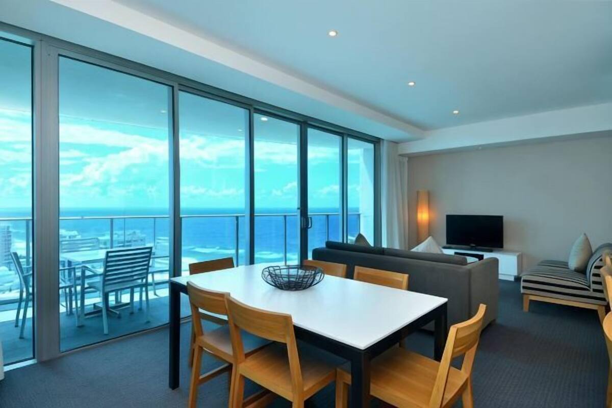 A modern hotel room with a balcony, a dining area, a sofa, and a TV.