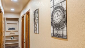 Un pasillo con un reloj en la pared, un letrero que dice 'HOME' y dos cuadros con relojes.