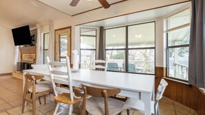 Un comedor con una mesa y sillas blancas, un ventilador de techo y ventanas amplias con persianas.