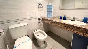 A modern bathroom with a toilet, bidet, sink, and mirror.