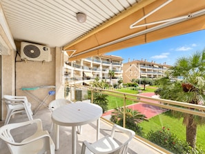 A balcony with a table and chairs, an air conditioning unit, and a view of a residential area with buildings and greenery.