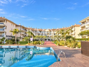 A hotel with a swimming pool, multiple balconies, and a clear sky.