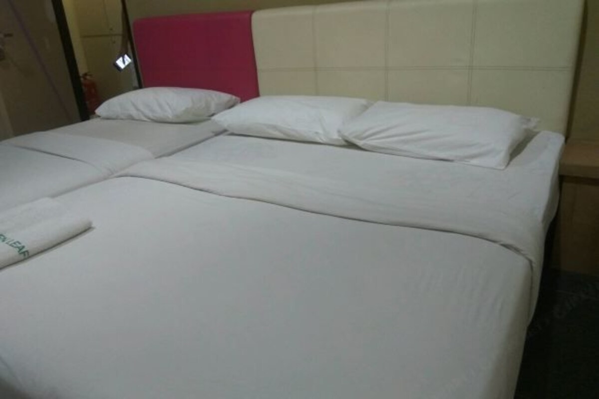 Ein Doppelbett mit weißen Leinentüchern, ein rosafarbenes Kopfteil und eine sichtbare Tür links.
