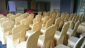 Een vergaderzaal met rijen stoelen bekleed met beige hoesjes, een whiteboard en een spreekgestoelte.