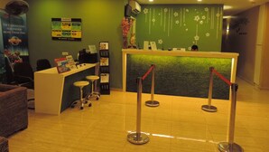 A reception area with a green wall, a reception desk, a phone, and a poster. - Golden Leaf Boutique Hotel (Johor Bahru)