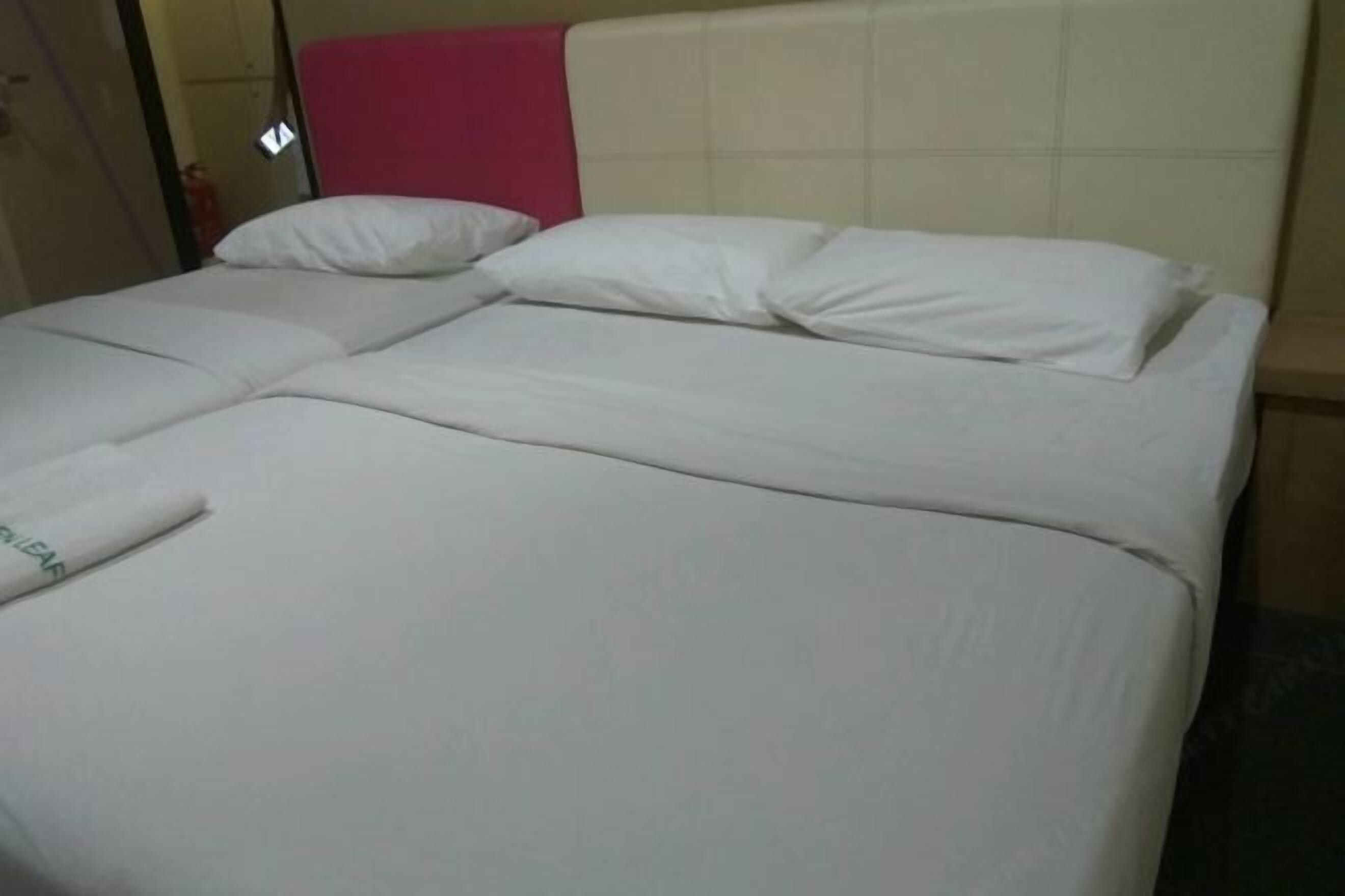 Una cama doble con ropa blanca, cabecera rosa y una puerta visible a la izquierda.