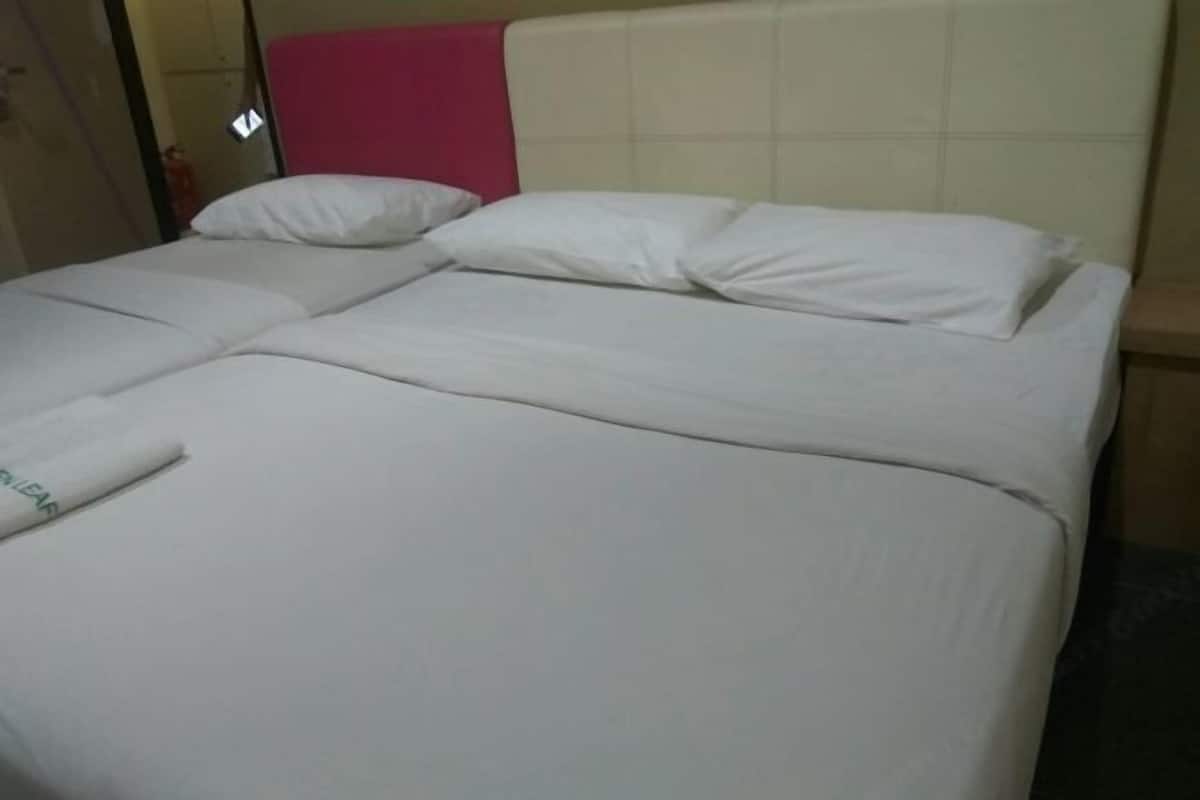 A double bed with white linens, a pink headboard, and a visible door to the left.