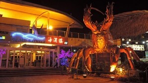 Een groot buitens beeld van een krab voor een gebouw met rieten dak en verlichte borden.
