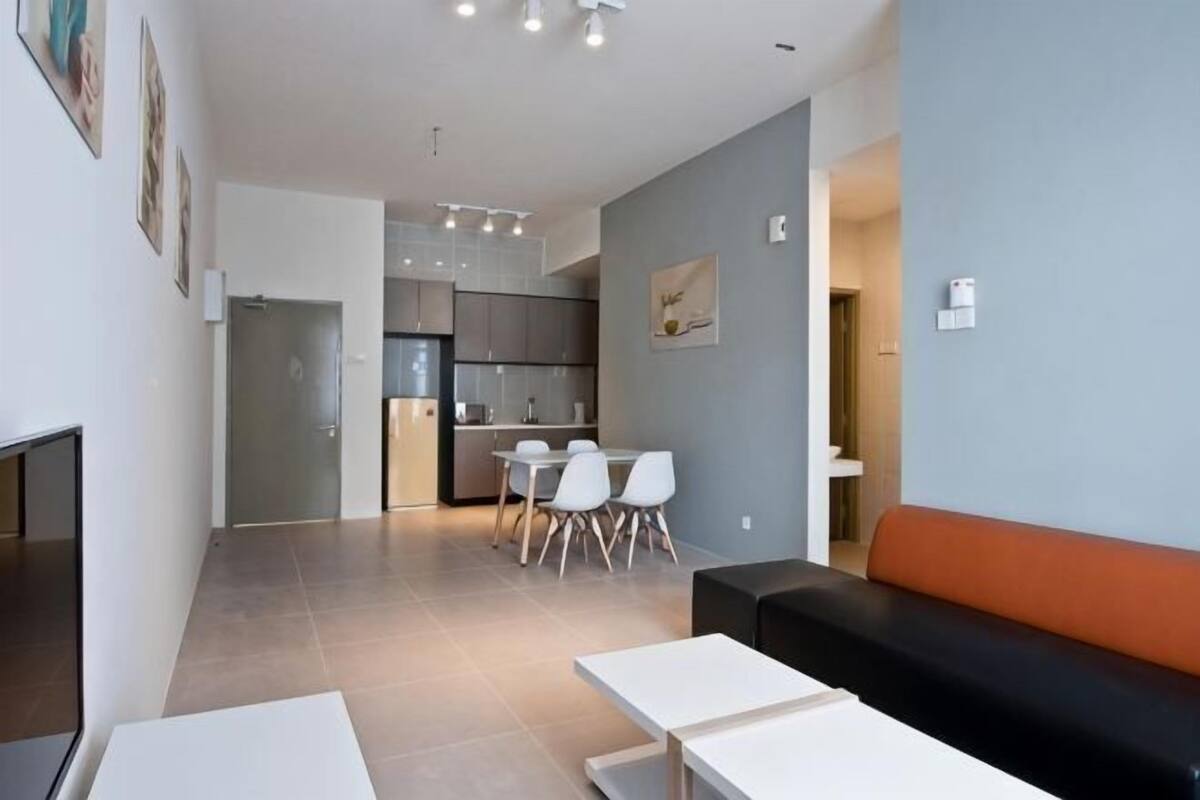 A modern living room with a sofa, a dining table with chairs, a kitchen area, and a hallway leading to a bathroom.