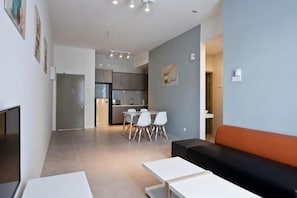 A modern living room with a sofa, a dining table with chairs, a kitchen area, and a hallway leading to a bathroom. - DreamScape Apartment @ Golden Hill (Brinchang)