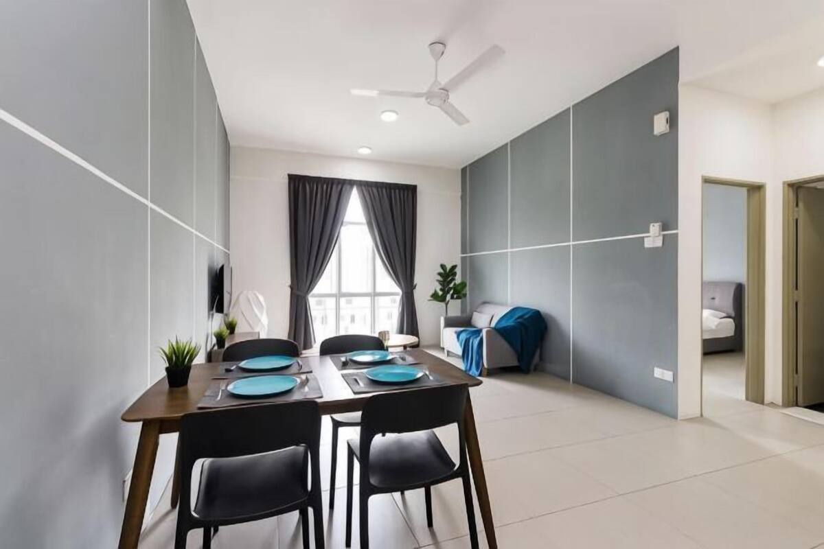 A modern dining area with a table set for four, a ceiling fan, and a view to a living area with a sofa and curtains.