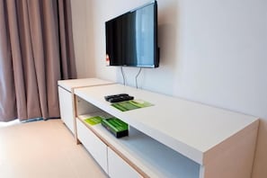 A room with a flat-screen TV mounted on the wall, a white desk with drawers, a remote control, and a green booklet on the desk. - DreamScape Apartment @ Golden Hill (Brinchang)