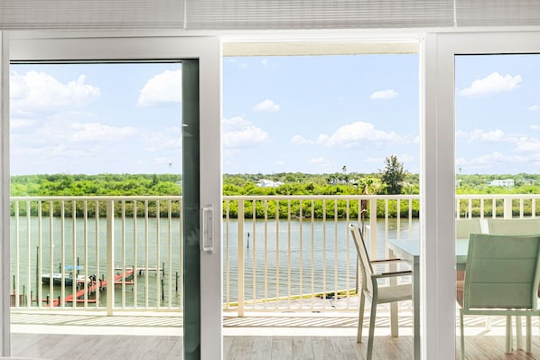 A balcony with a view of a lake, a table, and chairs.