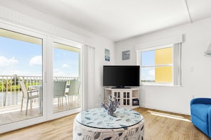 A modern living room with a flat-screen TV, a round glass table, and a blue sofa.