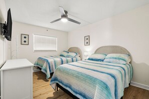 A bedroom with two beds, a ceiling fan, a TV mounted on the wall, and a window with blinds. - Holiday Villas III - 410 Stunning Condo Intracoastal View Balcony , heated pool! (Indian Rocks Beach)