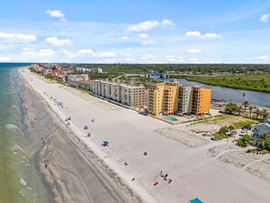 A coastal hotel with multiple floors, a beach, and a river in the background.