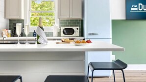 A modern kitchen with a central island, bar stools, a microwave, and a refrigerator. - The Double Up | The Quad in Park Circle (North Charleston)