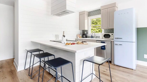A modern kitchen with a white island, bar stools, a built-in oven, and a refrigerator. - The Double Up | The Quad in Park Circle (North Charleston)