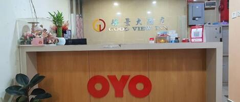 Una recepción con un panel de madera, el logo 'OYO', un cartel que dice 'GOO VIEW' y una planta en maceta.