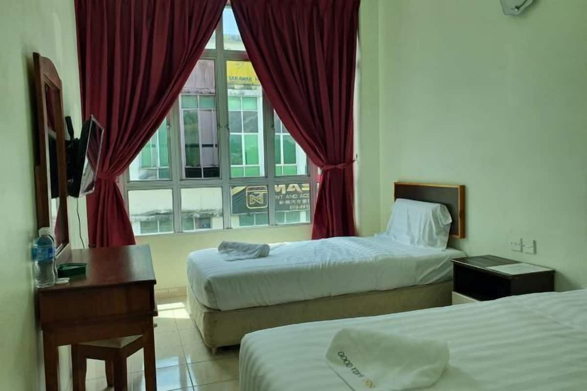 A hotel room with two beds, a desk, a chair, a window with curtains, and a wall clock.