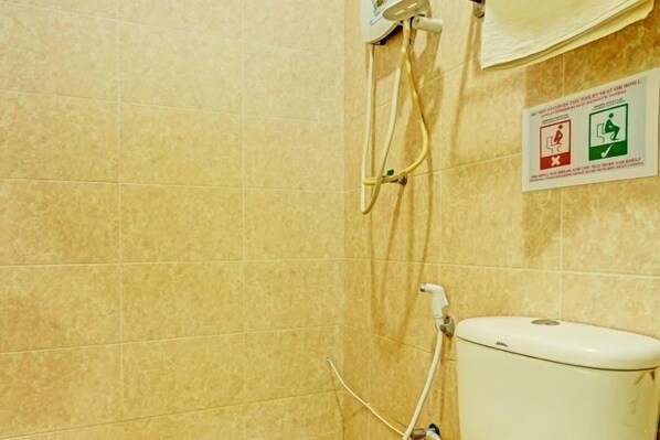 A bathroom with beige tiles, a toilet, a shower with a hose, and a sign indicating a toilet seat cover is required. - Hotel O Good View Inn (Sri Aman)