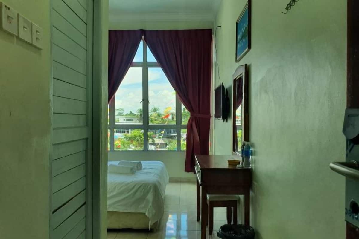 A room with a bed, a desk, a chair, a window with curtains, and a television on the wall.