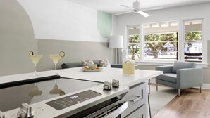 A modern kitchen with a built-in stove, a dining area with a table and chairs, and a view of the outdoors through large windows. - The Duo at the Quad in Park Circle (North Charleston)
