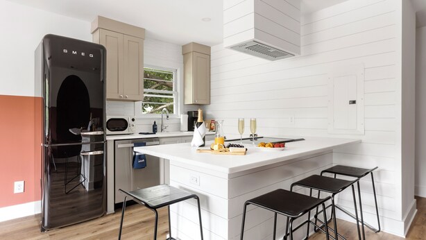 A modern kitchen with a large island, bar stools, a refrigerator, and a window. - The Duo at the Quad in Park Circle (North Charleston)