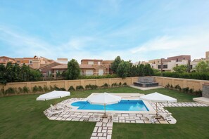 A backyard with a swimming pool, lounge chairs, and umbrellas.