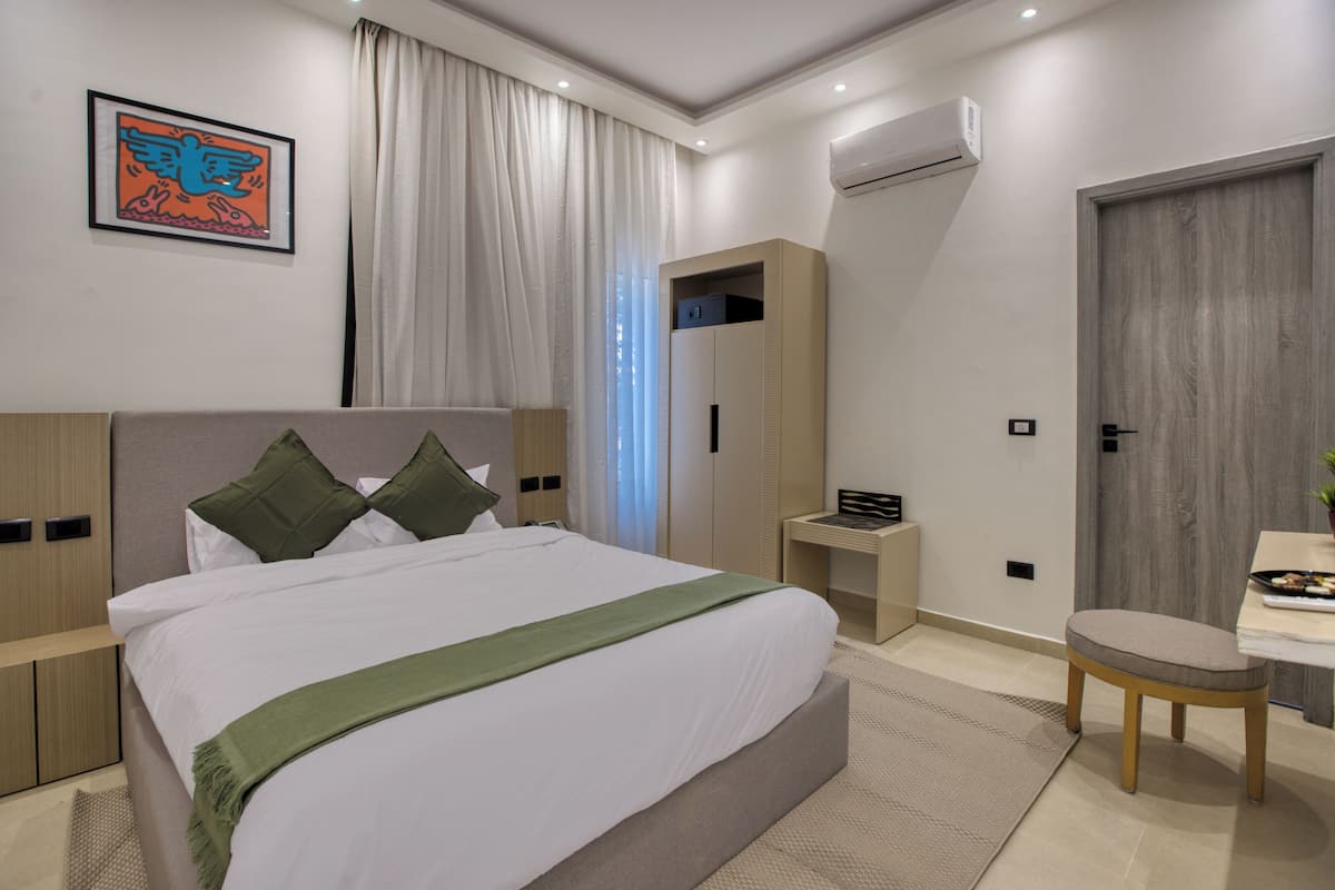 A modern hotel room with a large bed, a desk, a wardrobe, and an air conditioning unit.