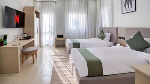 A hotel room with two beds, a desk with a flat-screen TV, a coffee maker, and a small table with a plant. - Seven Stays Zayed (Sheikh Zayed City)