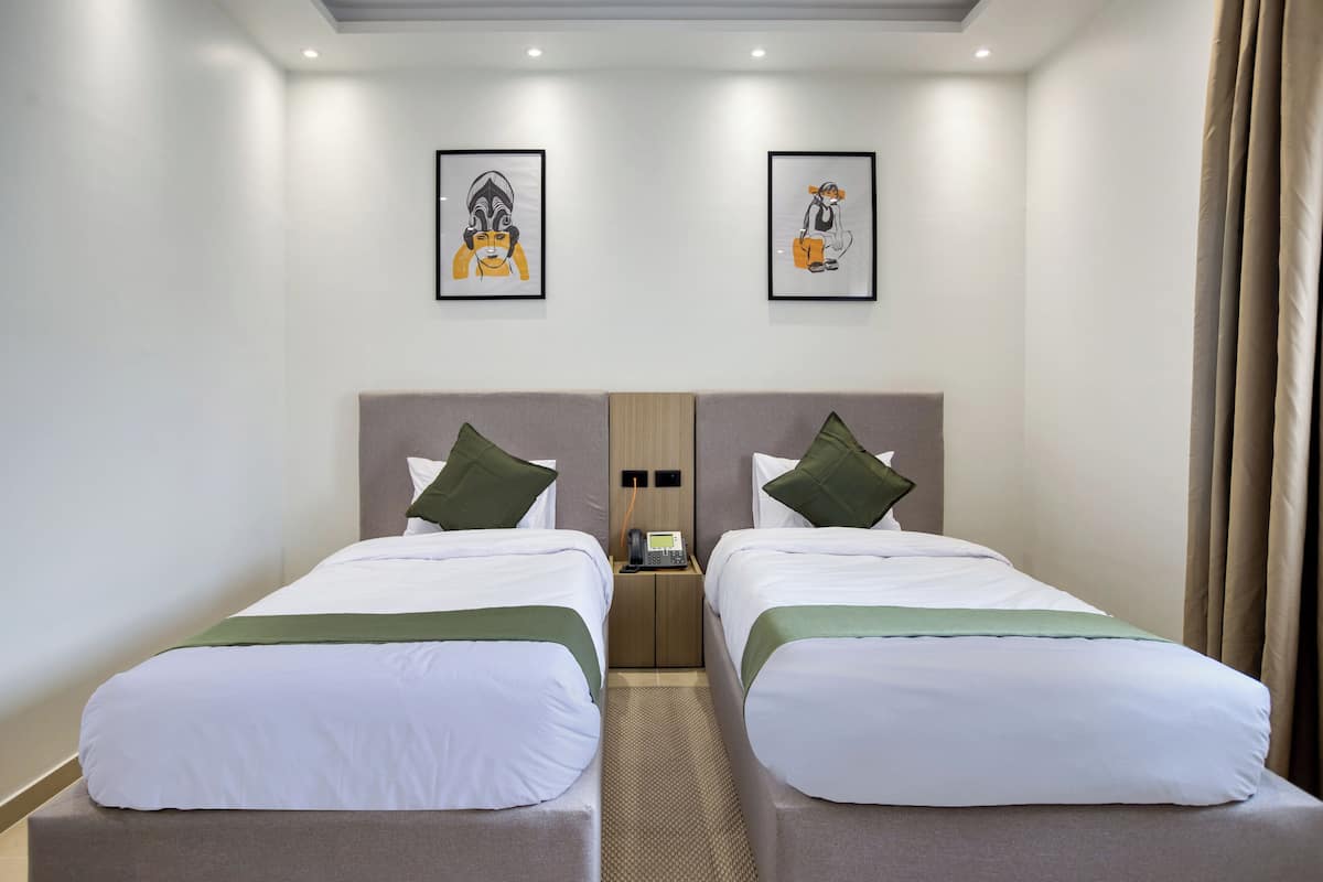 A hotel room with two beds, a nightstand with a phone, and artwork on the walls.