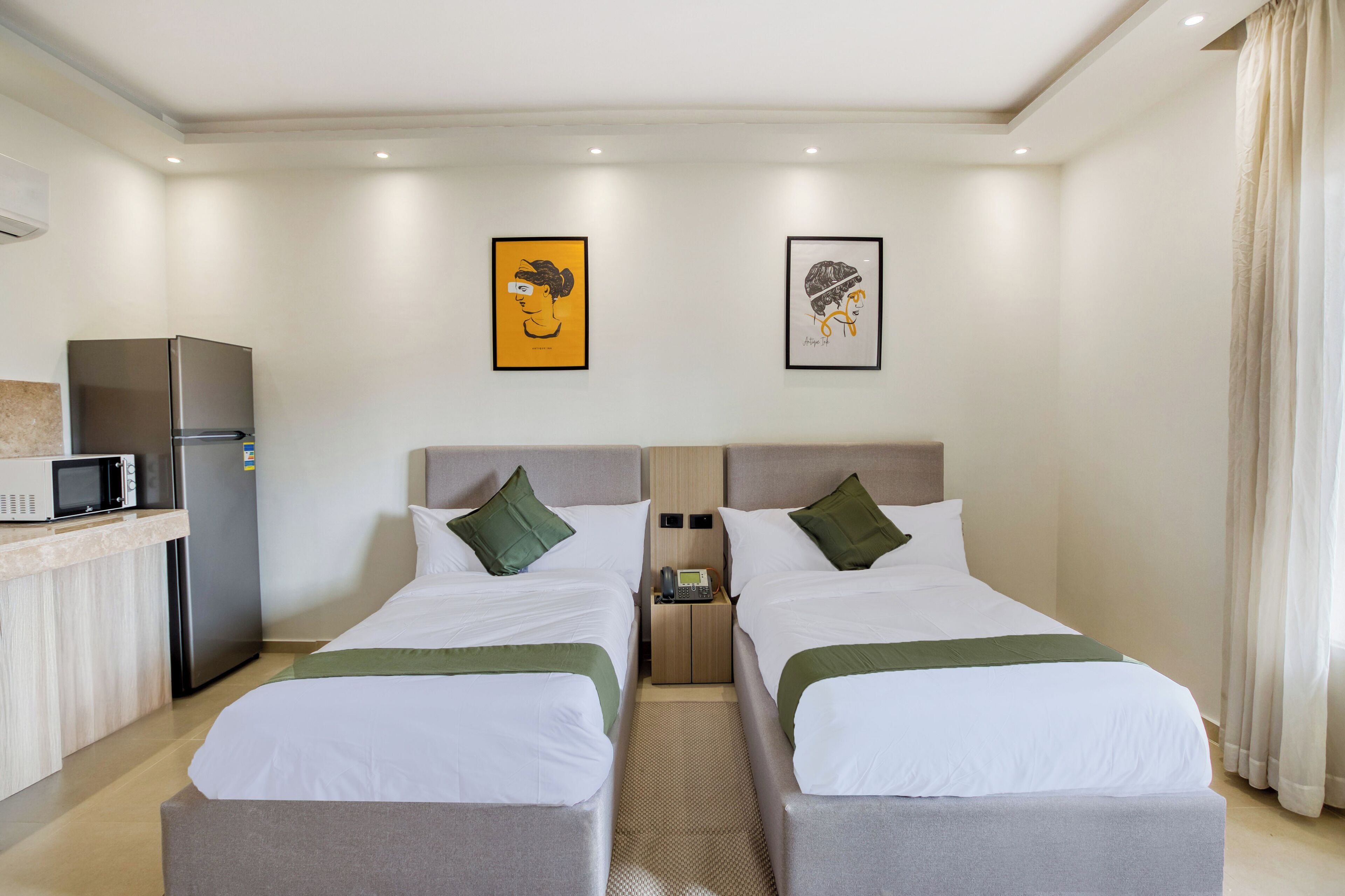 A hotel room with two beds, a kitchenette, and artwork on the walls.