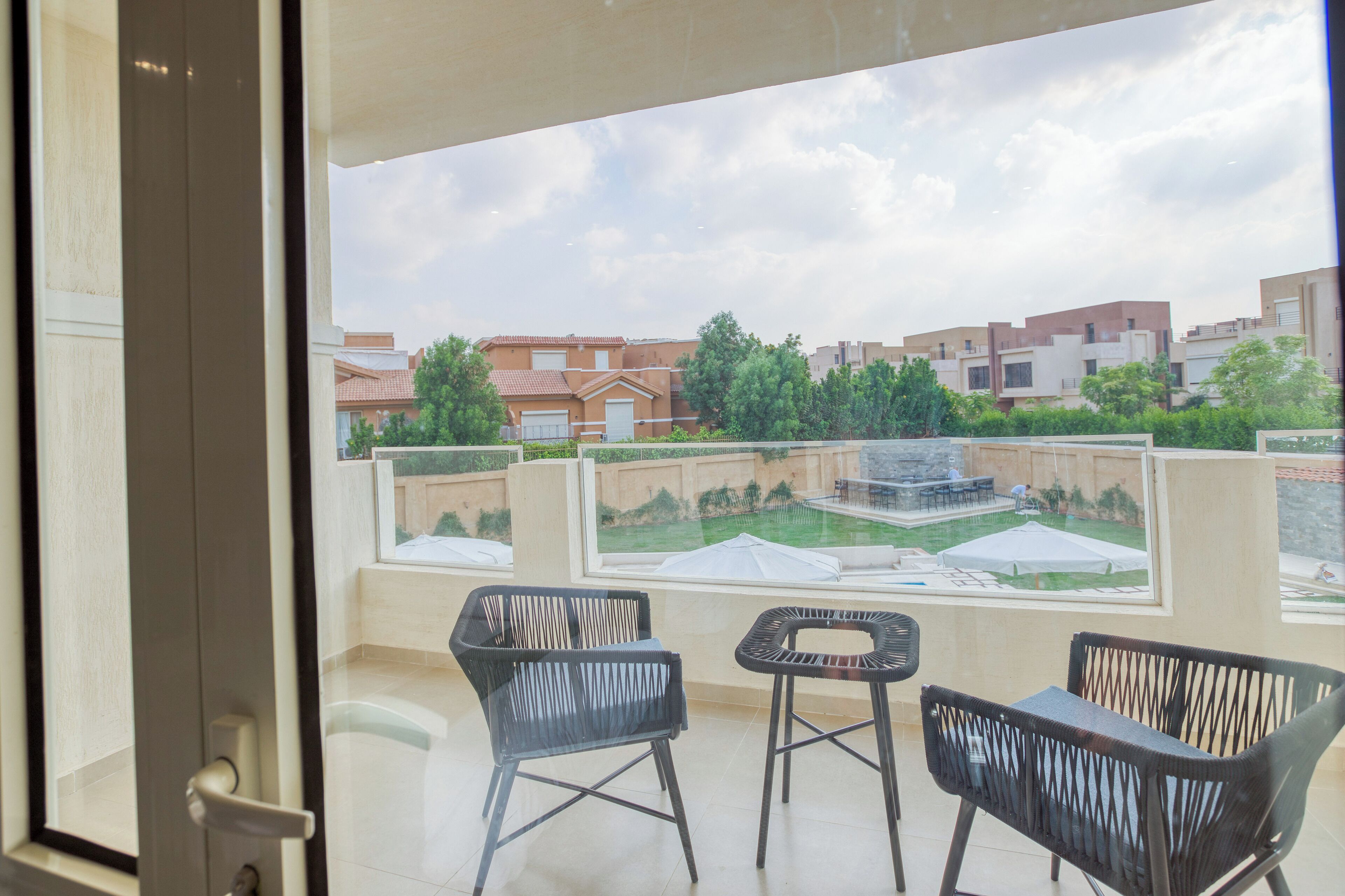 Un balcón con dos sillas negras y una mesita, con vistas a una zona residencial con casas y vegetación.