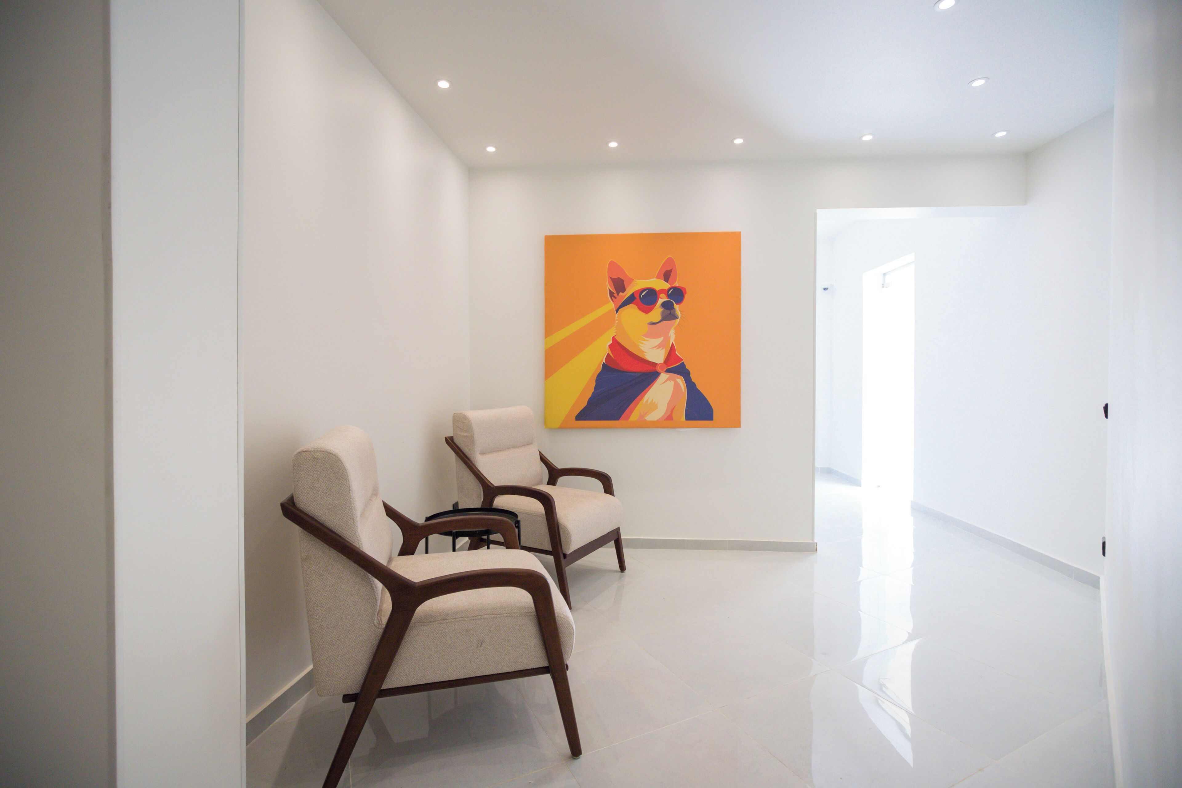 Un couloir moderne avec trois fauteuils beiges et un tableau abstrait aux couleurs vives accroché au mur.