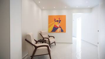 Un couloir moderne avec trois fauteuils beiges et un tableau abstrait aux couleurs vives accroché au mur.