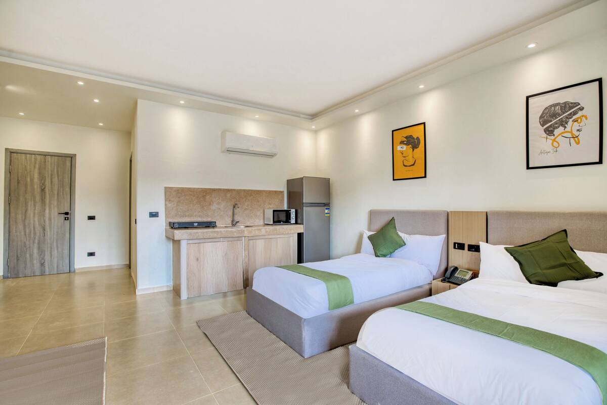 A hotel room with two beds, a kitchenette, and a bathroom.