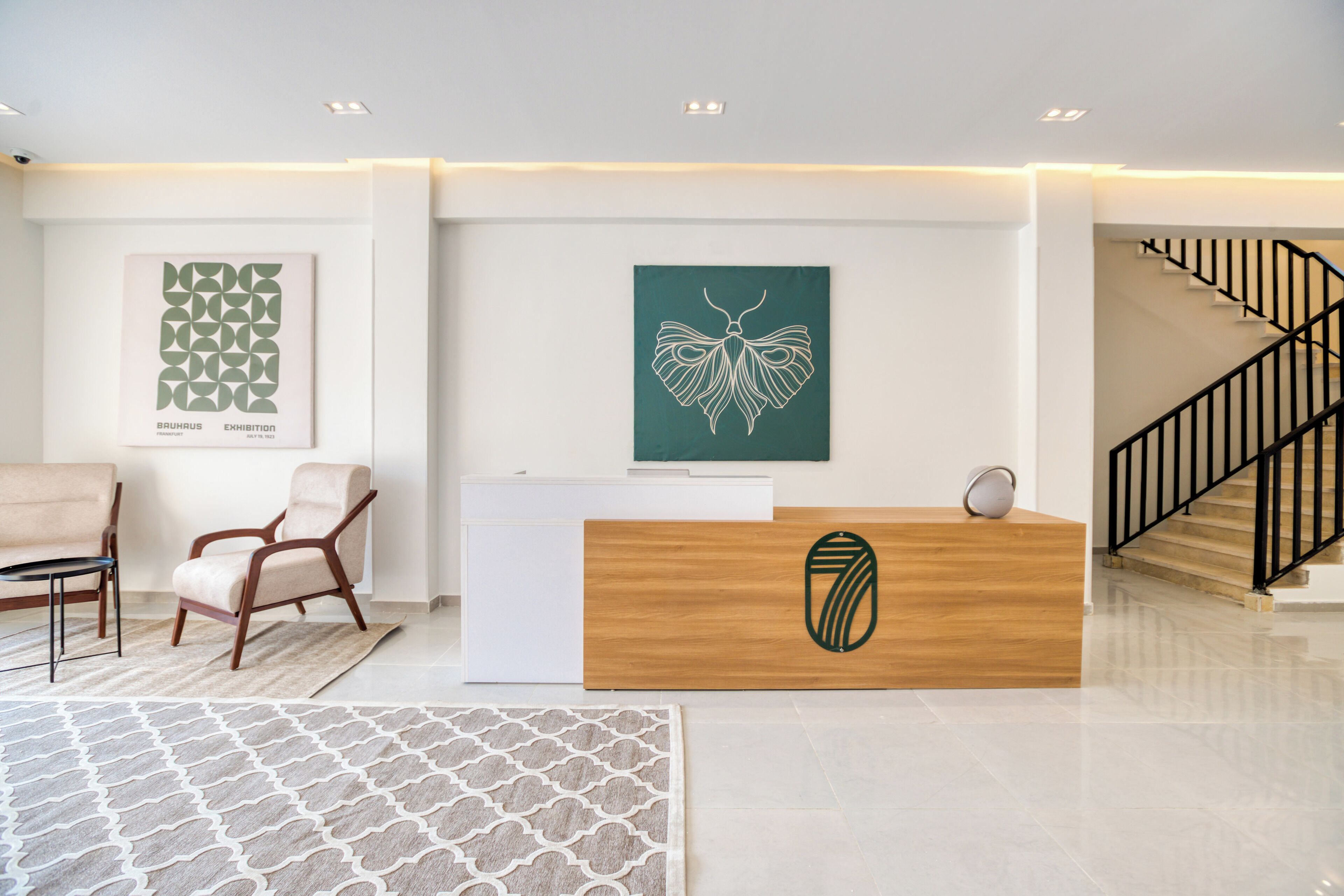 Un área de recepción con un escritorio de madera, dos sillas, un tapete estampado y obras de arte en las paredes.