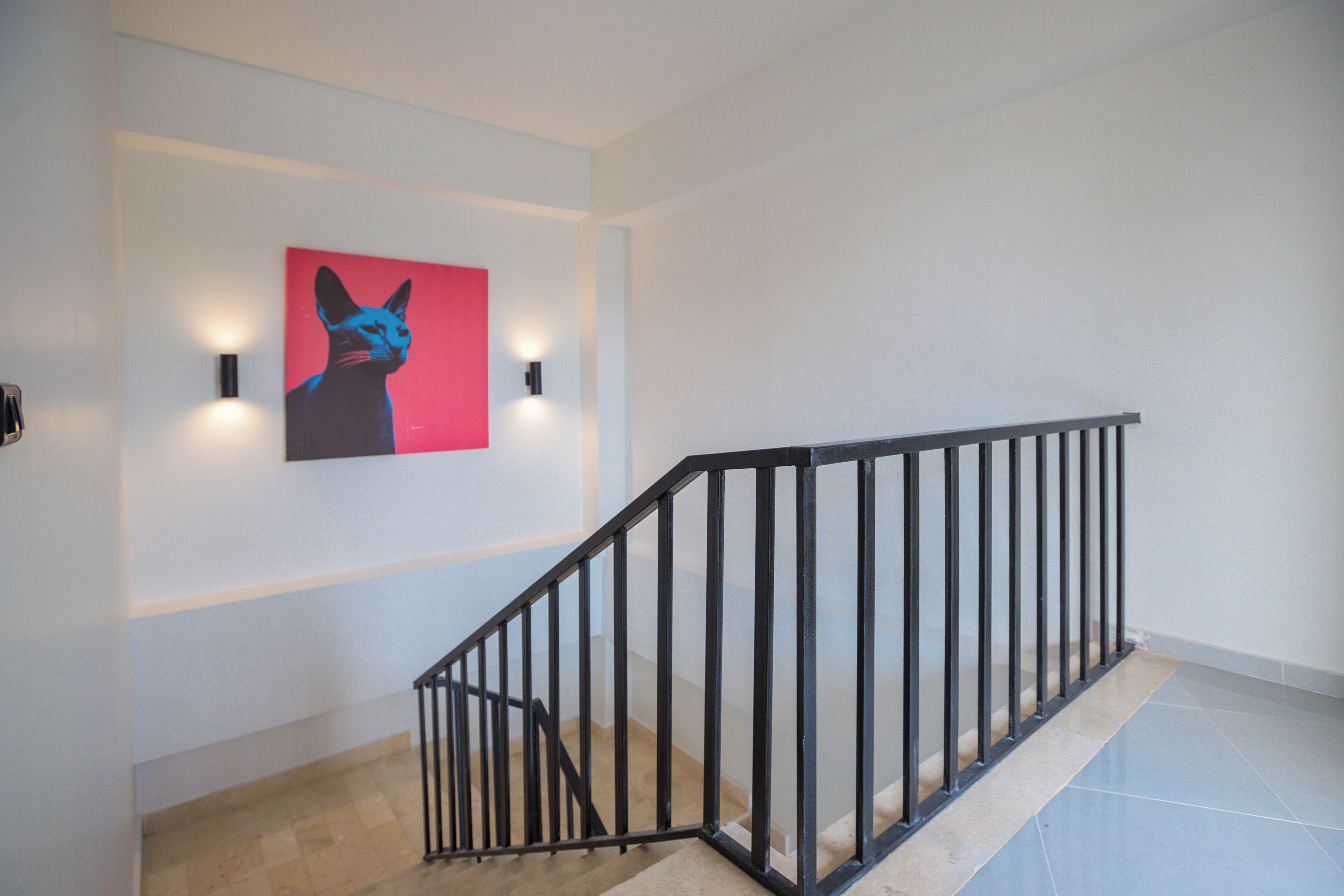 A staircase with a black metal railing, a wall-mounted light fixture, and a framed artwork depicting a cat.